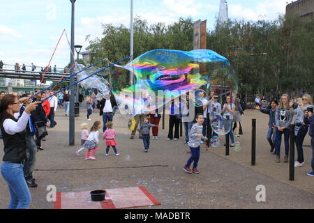 Street performer making giant soap bubbles with sticks and string on the South Bank, River Thames, London, England, UK, PETER GRANT Stock Photo
