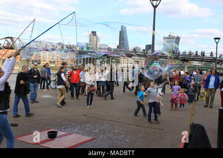 Street performer making giant soap bubbles with sticks and string on the South Bank, River Thames, London, England, UK, PETER GRANT Stock Photo