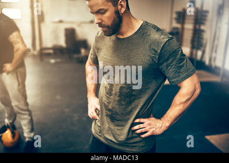 Fit young man in sportswear standing with his hands on his hips in a gym sweating after a workout session Stock Photo