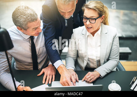 Mature manager and two corporate colleagues discussing work together on a laptop during a meeting in a modern office Stock Photo