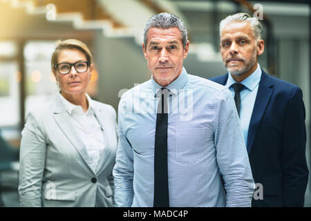 Focused mature businessman standing with two colleagues in the lobby of a modern office building Stock Photo