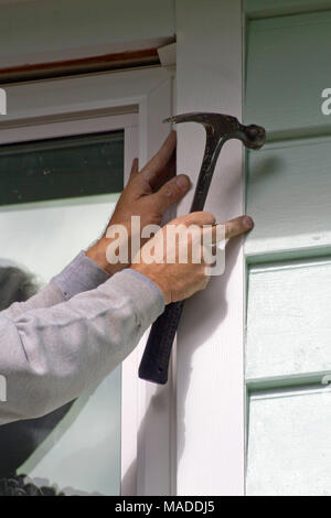 Close up of a man's hands holding a hammer as he in installs a new window and screen on a sunny day Stock Photo