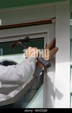 Close up of a man's hands wielding a hammer as he in installs a new window and screen on a sunny day Stock Photo