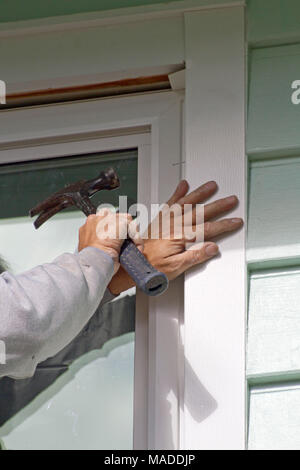 Close up of a man's hands holding a hammer as he in installs a new window and screen on a sunny day Stock Photo