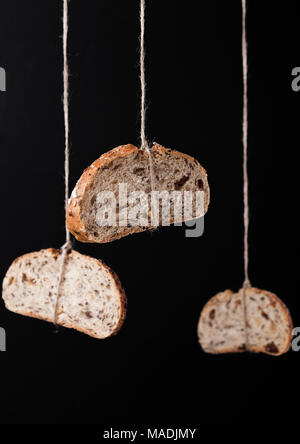 Freshly baked bread with oats hanging on rope on black background Stock Photo