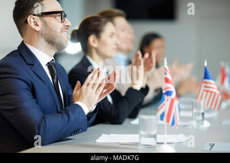 Young delegate and his colleagues clapping hands to speaker at political conference or summit Stock Photo
