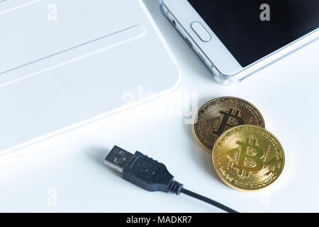 Bitcoins on a white table next to the tablet and smartphone Stock Photo