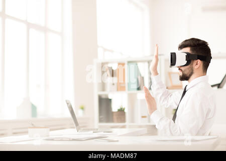 Businessman using VR glasses sitting at table in office taking break from work Stock Photo