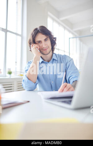 Portrait of businessman having a conversation on the phone and making notes at the table Stock Photo
