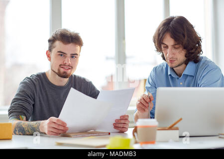 Portrait of two partners sitting with documents and using laptop Stock Photo