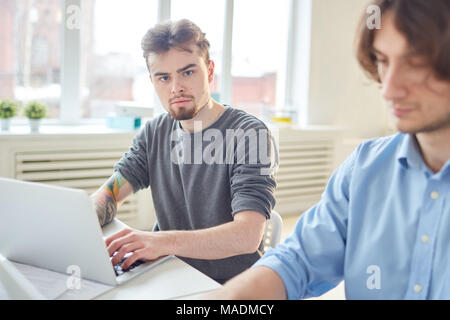Casual businessman using his laptop for work. He is sitting together with his coworker Stock Photo
