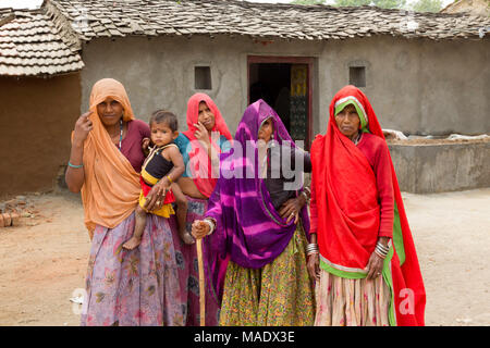 Four women with covered heads wearing brightly coloured saris and a child standing outside mud huts in a village near Shahpura, Rajasthan, India.