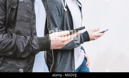 two unrecognizable mobile phone addicted male teenagers using smartphone Stock Photo