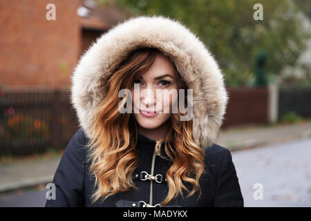 young woman wearing winter coat with fake fur hood outdoors Stock Photo