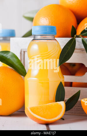 Plastic mini bottles of organic fresh orange juice with raw oranges in white wooden box Stock Photo