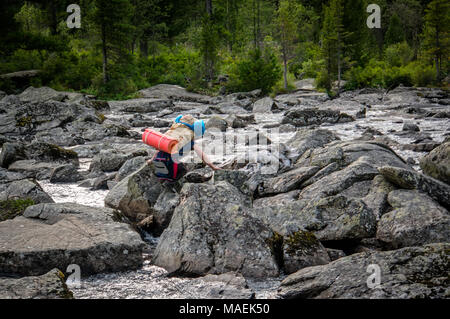 Hiker man with backpack crossing a river on stones in bulgarian mountains. Stock Photo