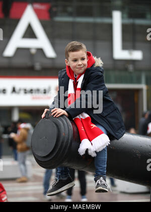 A young Arsenal fan sits on one of the cannons outside the ground prior to the Premier League match at The Emirates Stadium, London. Stock Photo