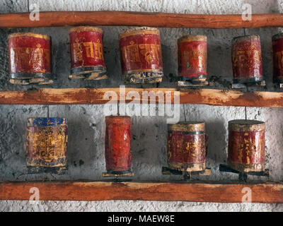 Traditional Buddhist ancient prayer drums: red cylinders in a wooden frame on the wall, inside the cylinders are religious Tibetan texts. Stock Photo