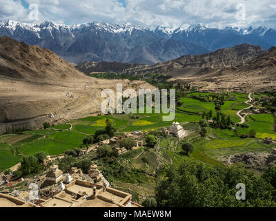 Mountain Tibetan village: among the high chains of ridges with snowy peaks are green fields with small houses and a white Buddhist stupa, the Himalaya Stock Photo