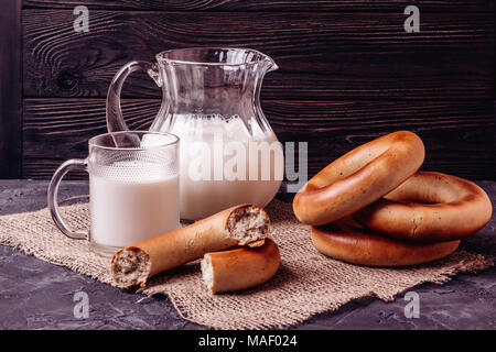 Glass jug with milk on a table next to a cup and bagels on a wooden wall background Stock Photo