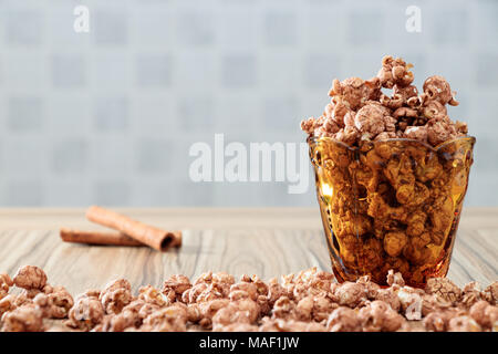 chocolate flavored popcorn in yellow glass and on the brown wood table with cinnamon background Stock Photo