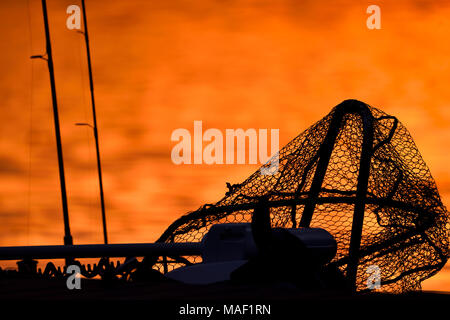 Silhouette of a trolling motor, landing net and fishing rods on a jetty in red sunset light on late October evening in Southern Finland. Stock Photo