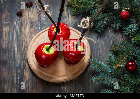 Red caramel apples on sticks on Dark wood background, with Christmas tree branches. Stock Photo