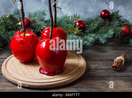 Red caramel apples on sticks on Dark wood background, with Christmas tree branches. Stock Photo