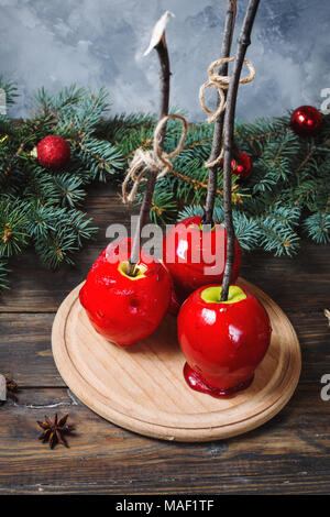 Red caramel apples on sticks on Dark wood background, with Christmas tree branches. Stock Photo