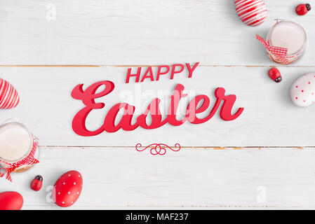 Happy Easter text in the middle surrounded with easter eggs, candles and ladybug decorations. White wooden table in the background. Stock Photo
