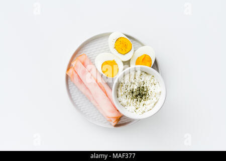 Breakfast, half boiled eggs, ham and fresh cheese sprinkled with dill. Top view, flat lay on white background. Stock Photo
