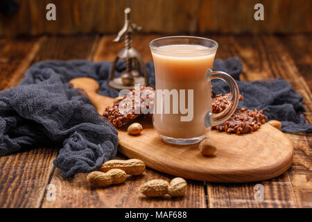 Tea with milk and cookies in glass cup on a beautiful board. Still life with tea, biscuits, nuts and an antique walnut. Delicious light breakfast. Stock Photo