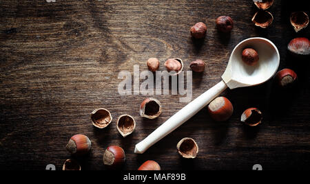 Nuts on a wooden table. Hazelnuts in the shells and shelled. A wooden spoon and nuts on brown table. Stock Photo