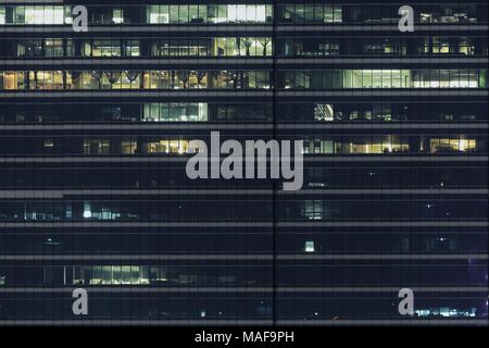 light illuminated from office room in a modern building. glass wall facade of a modern office tower. working in the night. Stock Photo