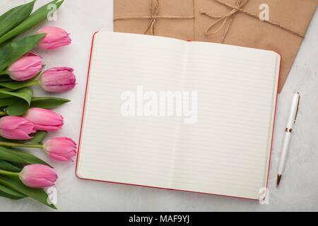 Blank note pad with pen, envelopes and pink tulips on light stone background. Stock Photo