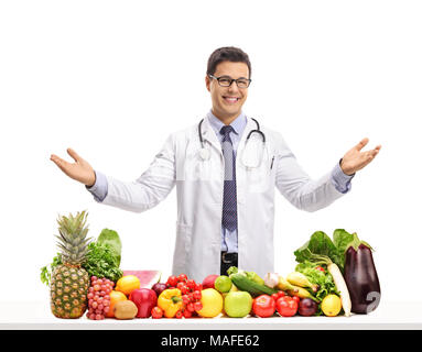 Doctor behind a table with fruit and vegetables gesturing with his hands isolated on white background Stock Photo