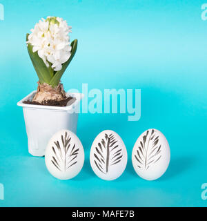 White hen eggs decorated for easter on a blue background. A black feather is drawn on the egg. Stock Photo