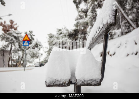 White snow covers a wooden bench. Wintertime, sky and nature at landscape with blurred snowy trees background. Close up view. Stock Photo