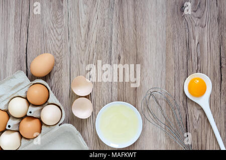 Fresh farm eggs on a wooden rustic background. Separated egg white and yolks, broken egg shells. Whipping eggs with whisk. Preparation of food from ch Stock Photo