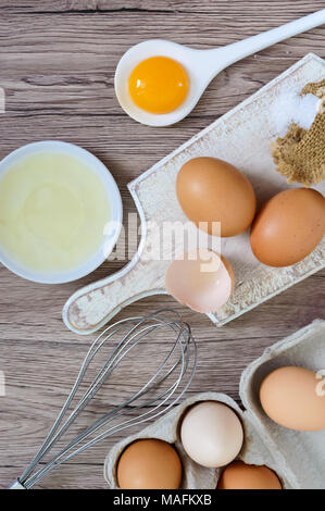 Fresh farm eggs on a wooden rustic background. Separated egg white and yolks, broken egg shells. Whipping eggs with whisk. Preparation of food from ch Stock Photo