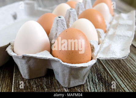 Fresh raw chicken eggs in carton egg box on wooden background. Close-up view on brown and white eggs. The main ingredient for many dishes. Stock Photo