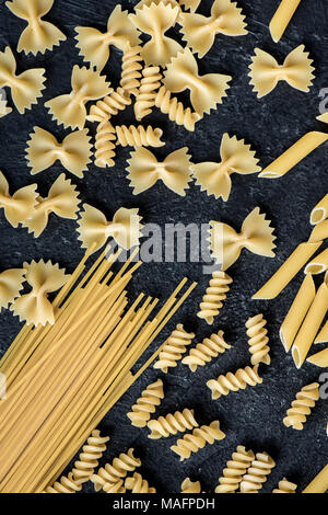 Assorted uncooked raw pasta on black background. Italian pasta: penne, farfalle, spaghetti, fusilli. Stock Photo