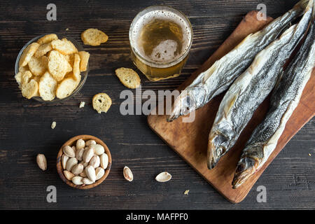Assorted snacks for beer: sun dried fish, nuts, salted croutons or crackers over wooden background, top view, copy space. Lager beer and snacks with d Stock Photo