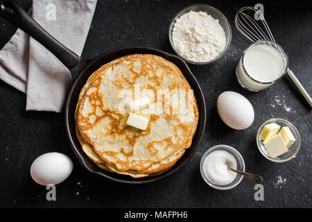 Homemade crepes with butter in cast iron pan and ingredients over rustic black background with copy space - cooking fresh homemade breakfast crepes pa Stock Photo