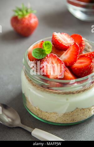 Strawberry cheesecake in glass jar with fresh strawberries and cream cheese  on grey concrete background. Healthy homemade organic dessert. Stock Photo