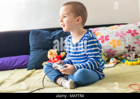 Cute boy playing video game console while sitting on sofa at home. Smiling and feeling happy. Stock Photo