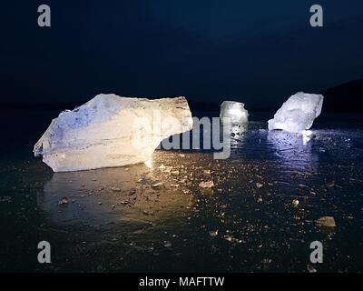 Arctic ice. A large piece of natural ice on a green blue flat ice of frozen lake, water bubbles texture. Shiny detail inside wonderful of transparent. Stock Photo