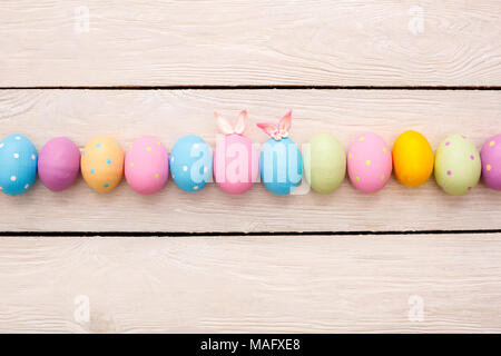 Easter objects colorful eggs isolated on wooden background in a row in the middle decorated with small cute bunny ears and paper butterfly top view Stock Photo