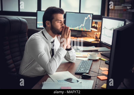 Young bearded man trader at office sitting at table looking at monitors thoughtful making strategy Stock Photo