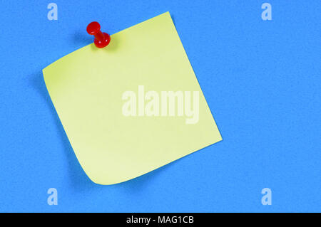 Yellow sticky note pinned to blue paper. Stock Photo